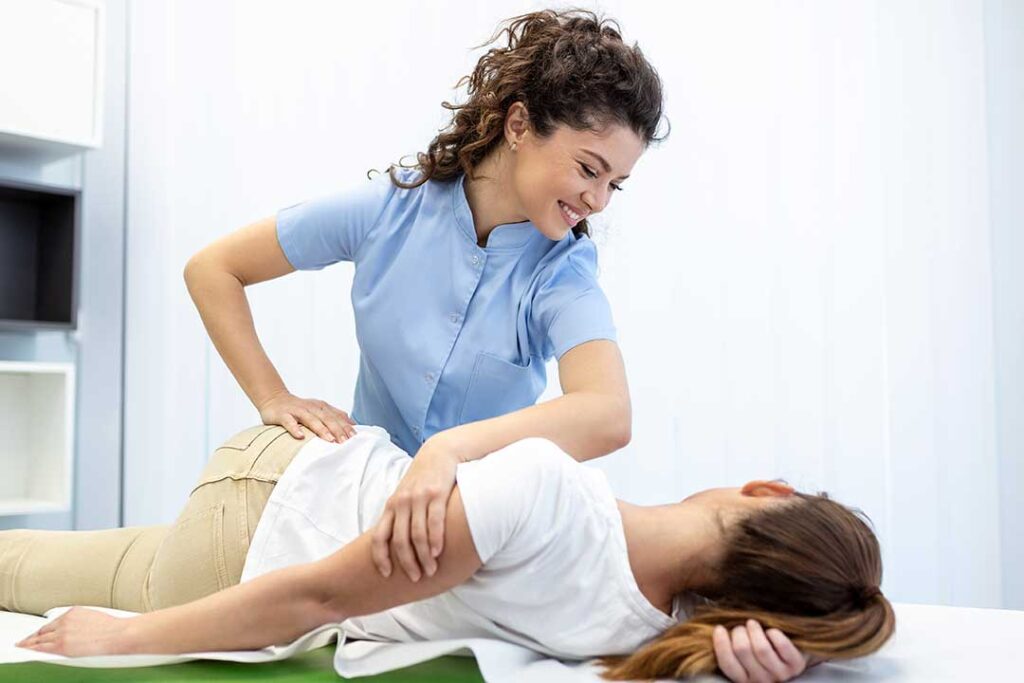 A chiropractor discusses a patient’s back movement beside an examination table in a bright clinic room.